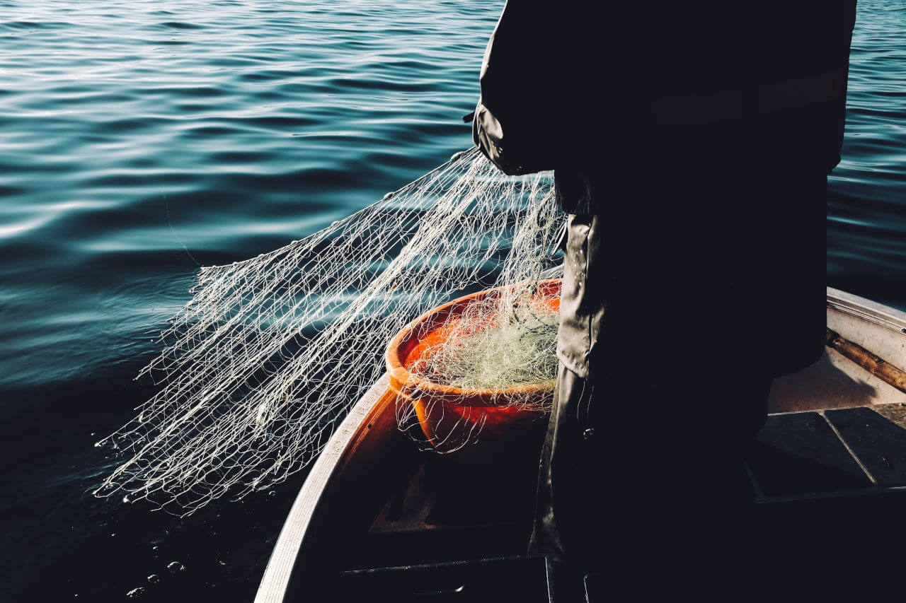 Ein Mensch auf einem kleinen Holzboot legt ein Fischernetz aus